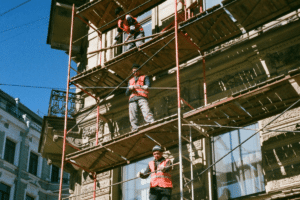Three construction workers stand atop scaffolding attached to a building that is being rennovated.