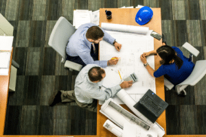 A team of professionals sits around a building plan laid out on a table.